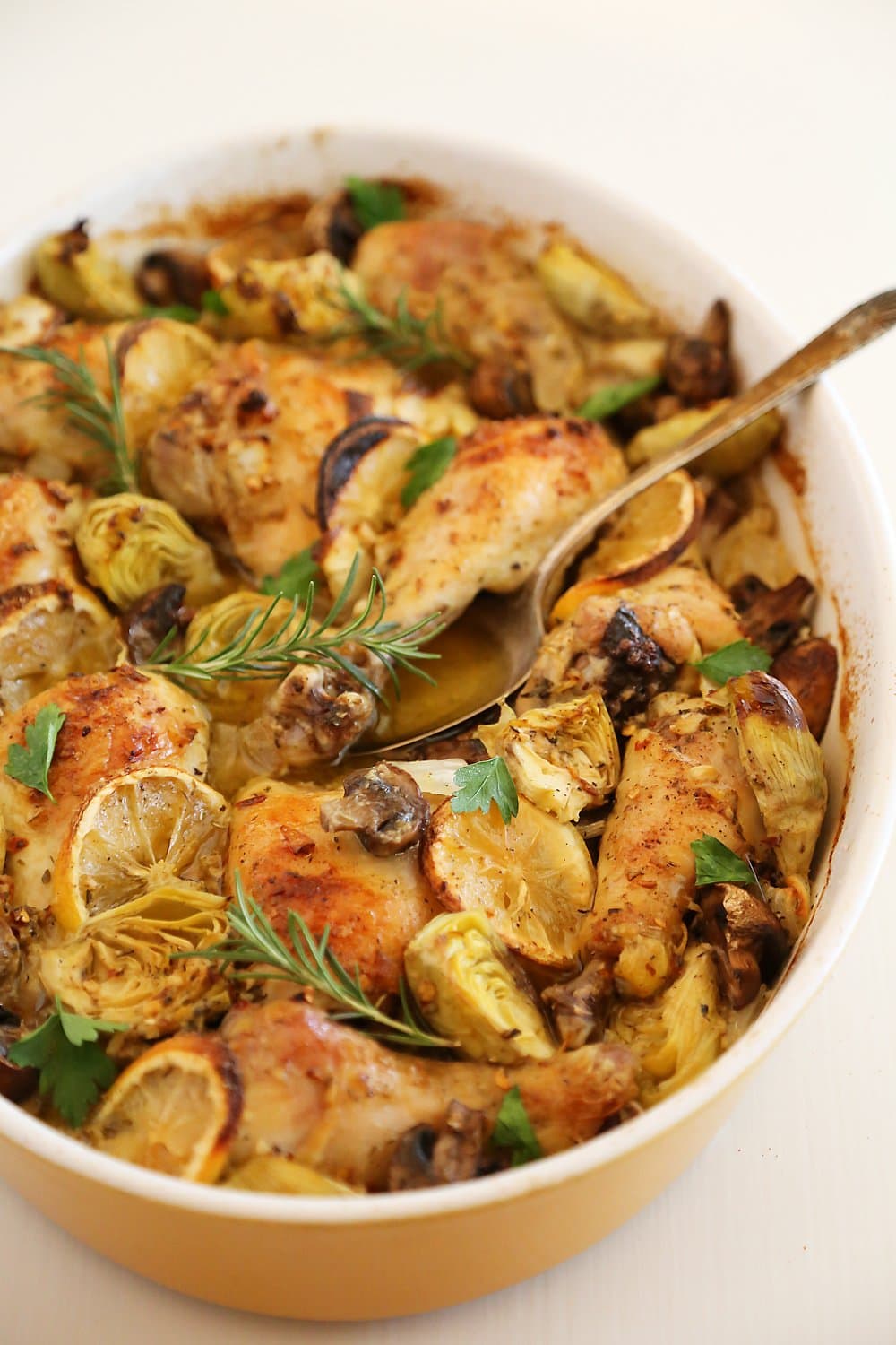 Oven roasted chicken with artichoke hearts, mushrooms and lemons in an oval dish.