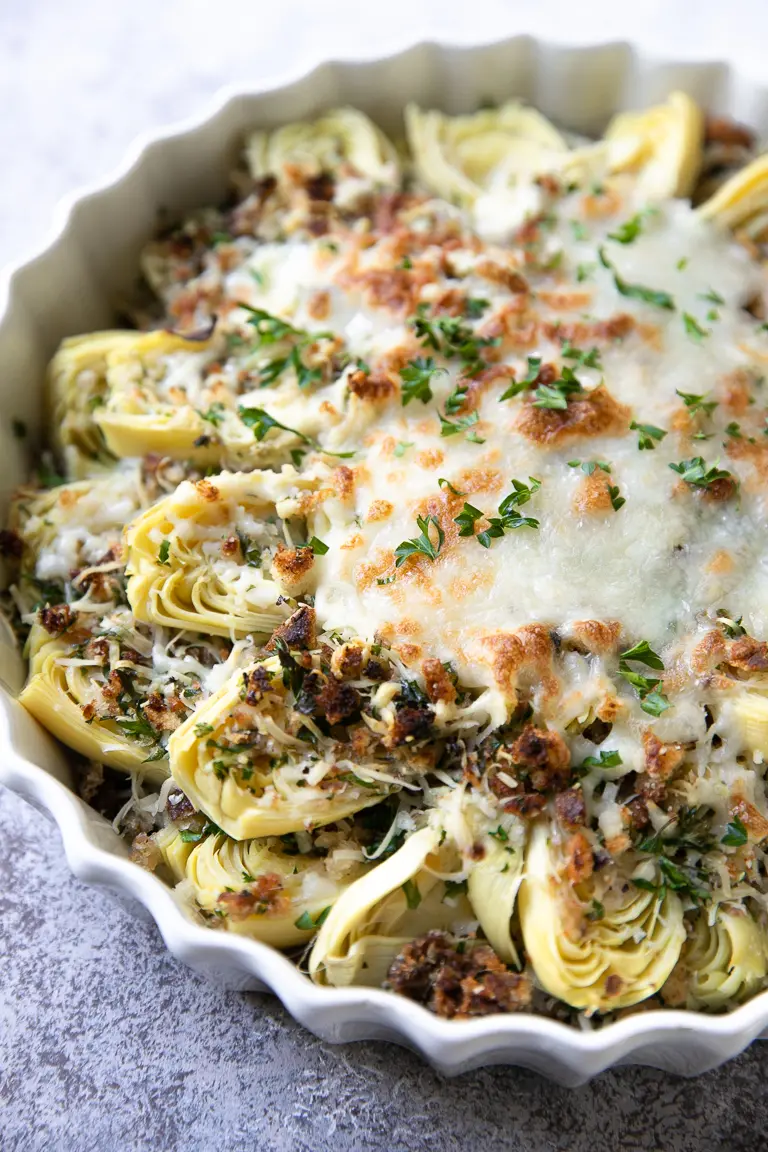 Baked artichokes with parmesan and breadcrumbs in a white dish.