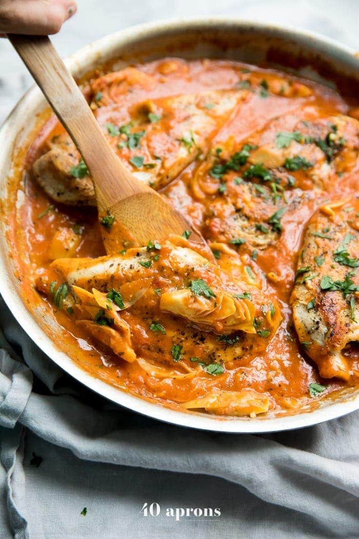 creamy tomato artichoke chicken in a skillet with a spoon lifting it out.
