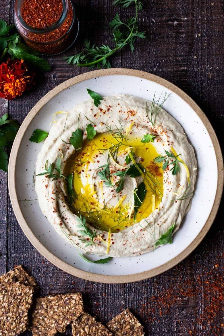 overhead view of a bowl of lemony artichoke white bean hummus drizzled with oil and topped with herbs.