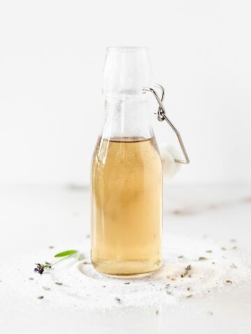 lavender syrup in a glass bottle surrounded by sugar and lavender buds.