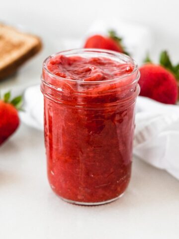 low sugar strawberry jam in a jar with strawberries around it.