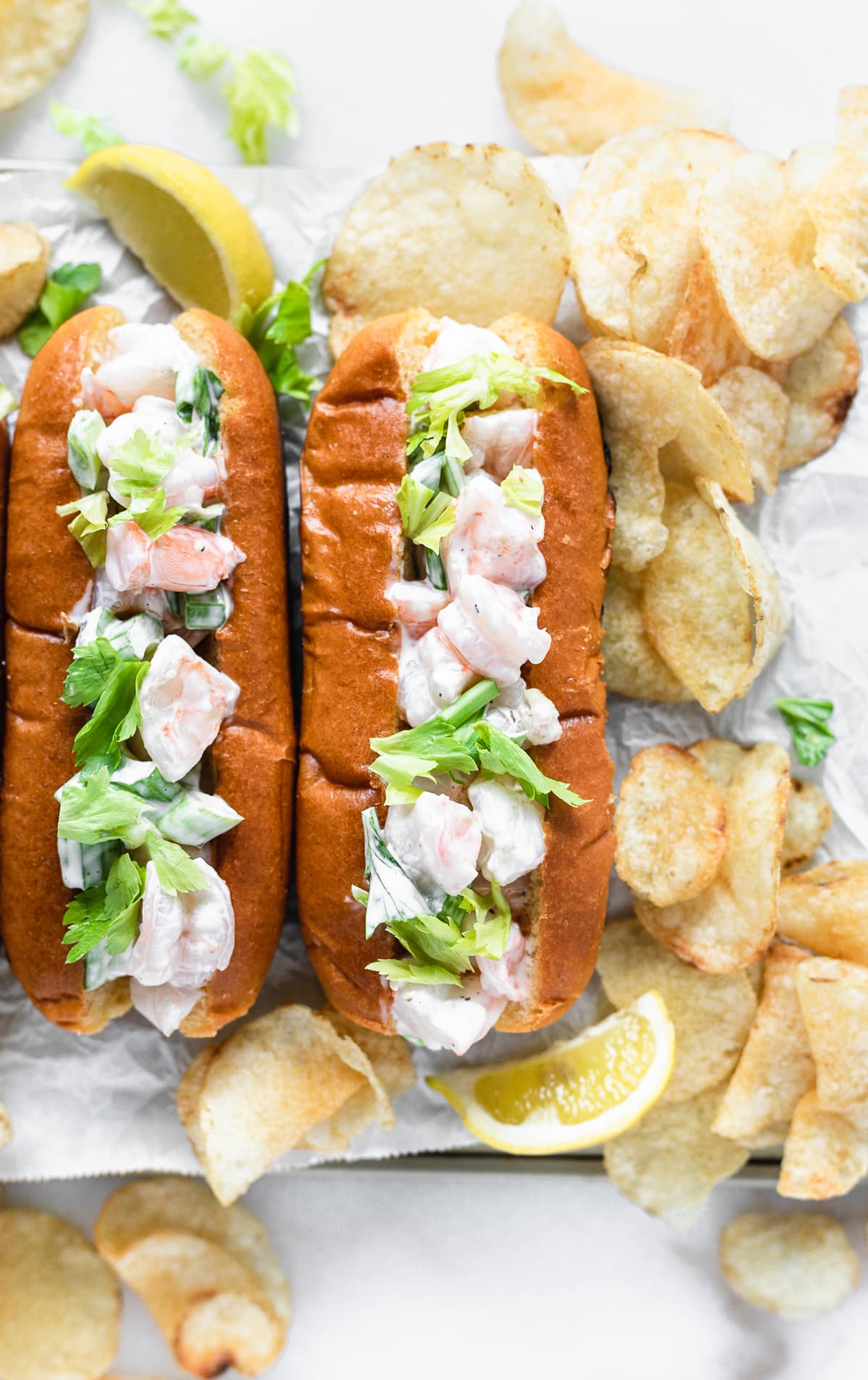 overhead view of two new england shrimp rolls with potato chips around them.