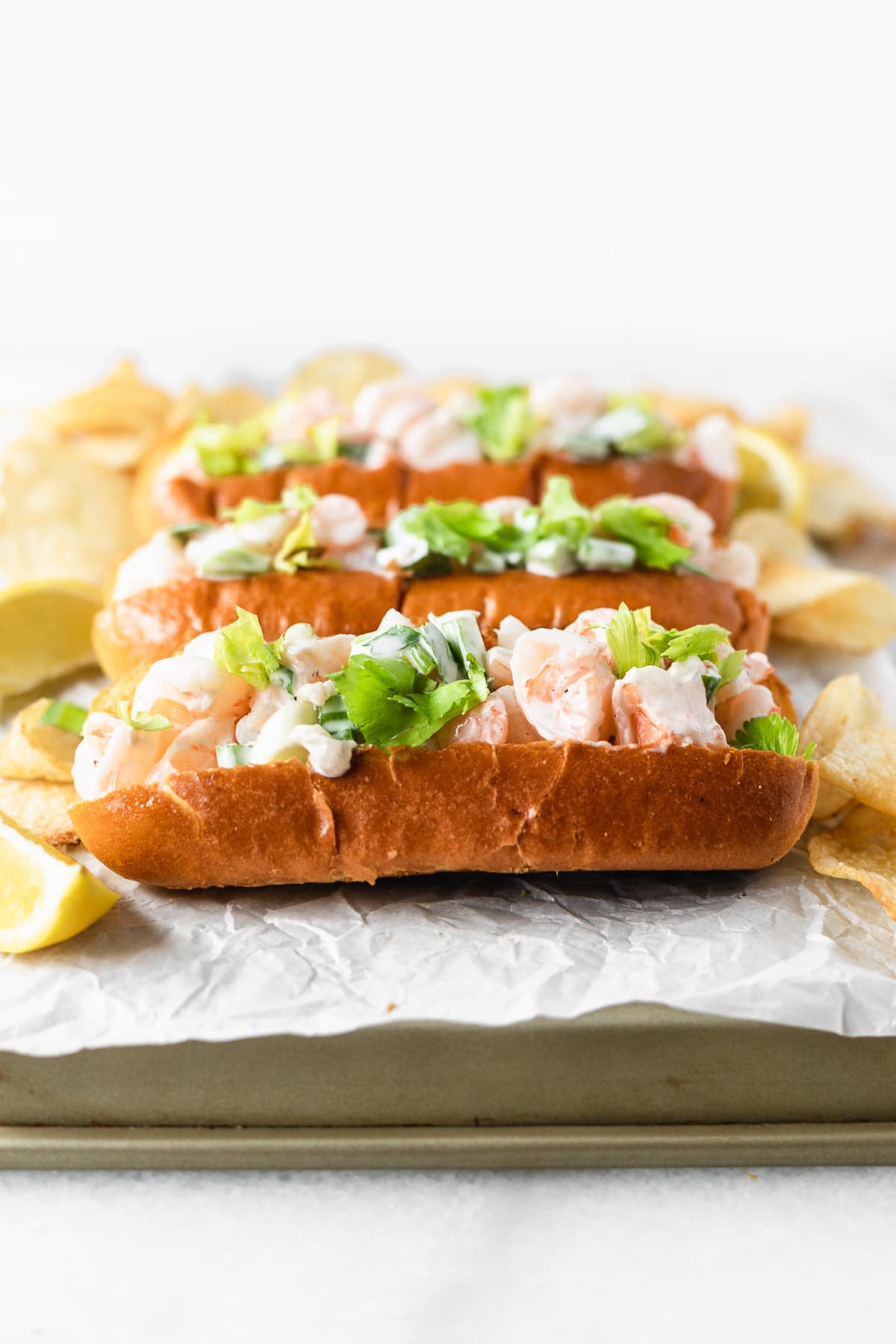 new england style shrimp rolls on a parchment lined tray with lemon wedges and potato chips.