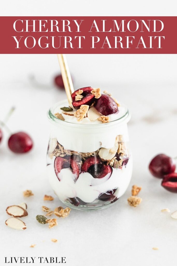 cherry almond yogurt parfait in a glass jar with a gold spoon in it with text overlay.